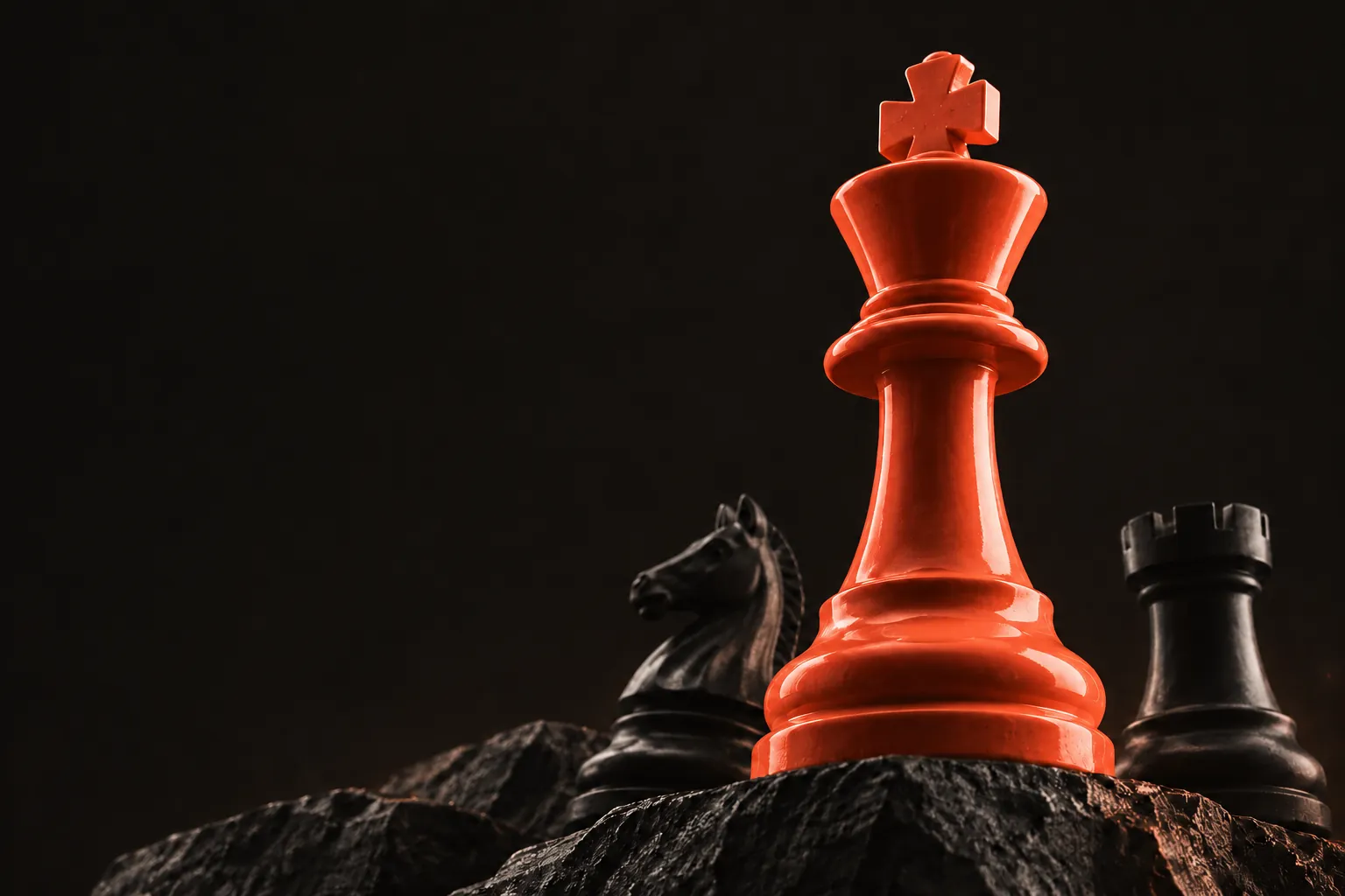 Un roi d’échecs corail se dresse sur un rocher, entre un cavalier et une tour noirs.